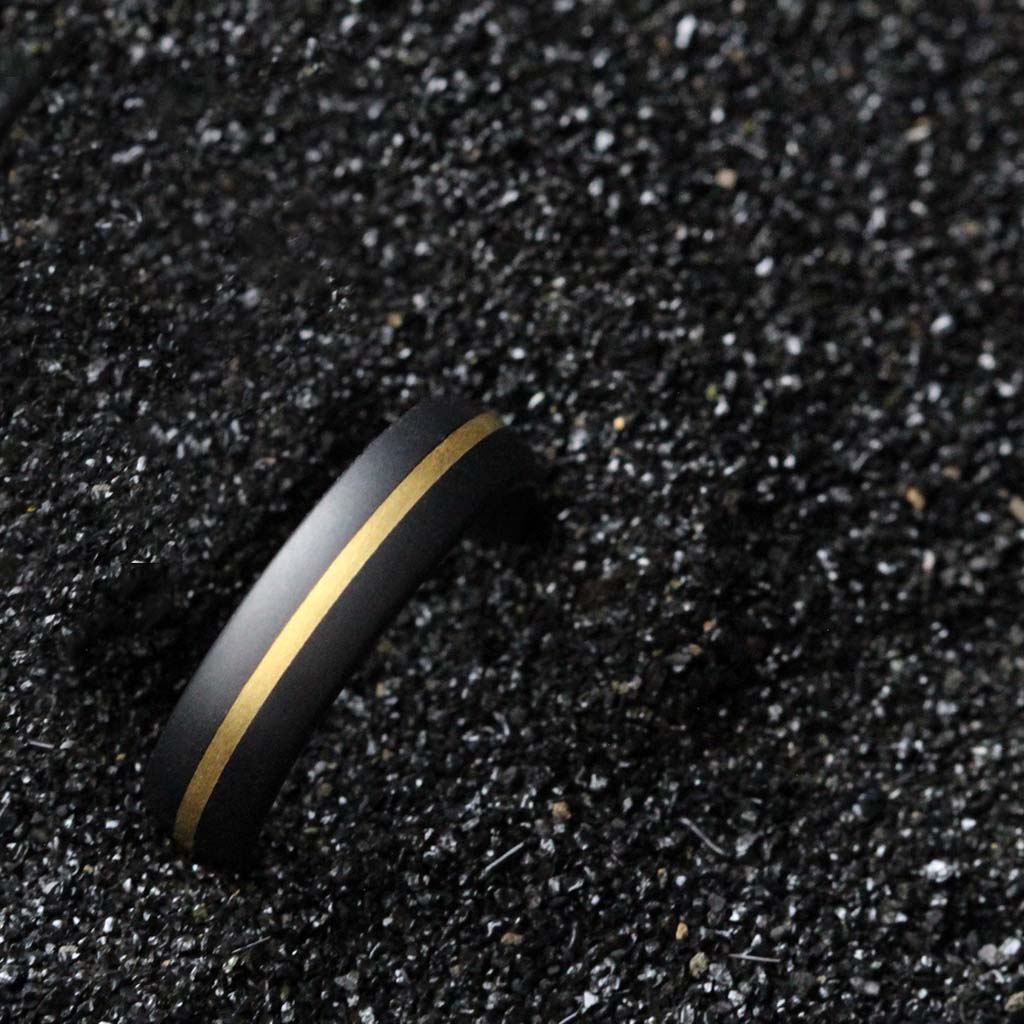 Black ring with a gold stripe on a dark gravel background