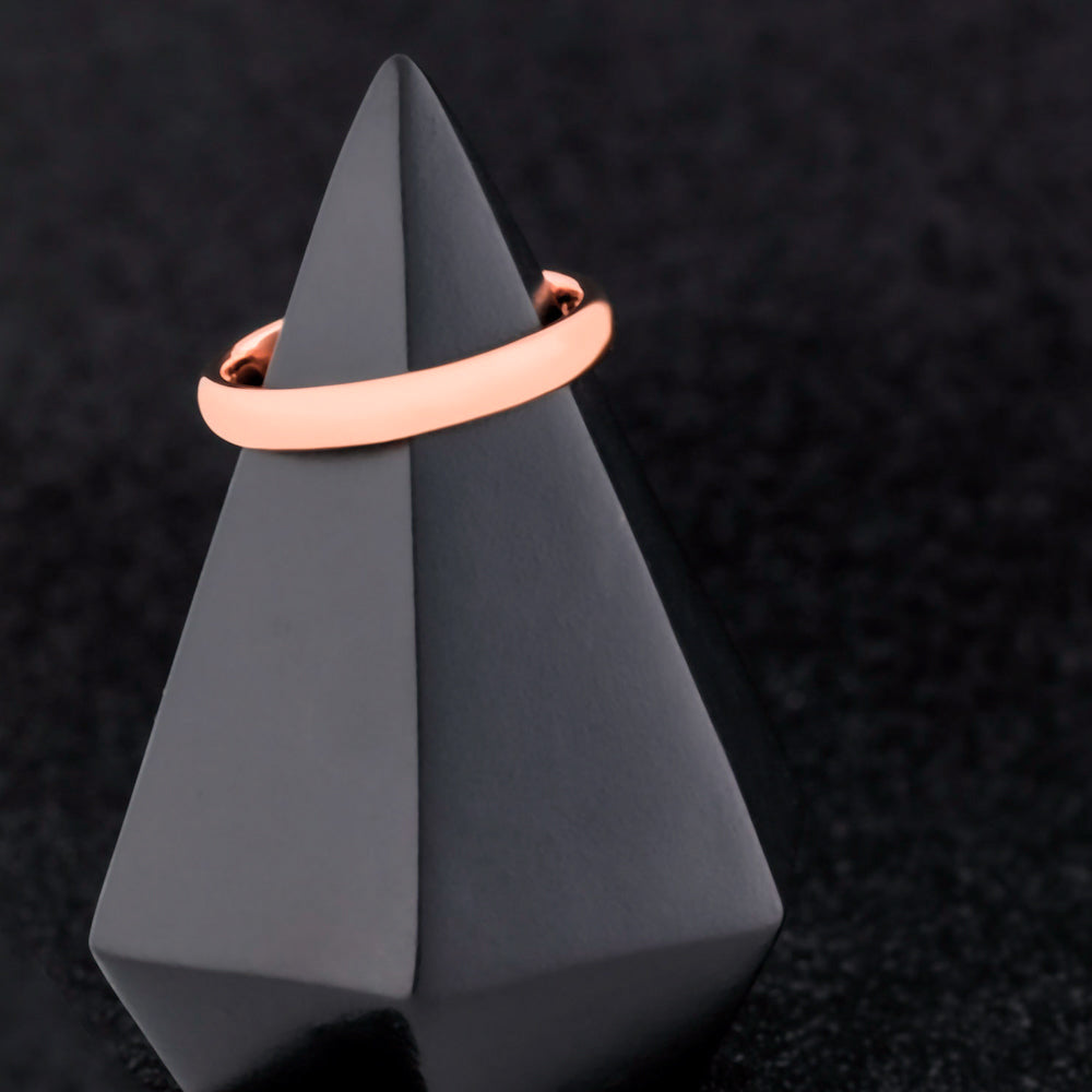 Rose gold ring on a gray geometric stand against a black textured background