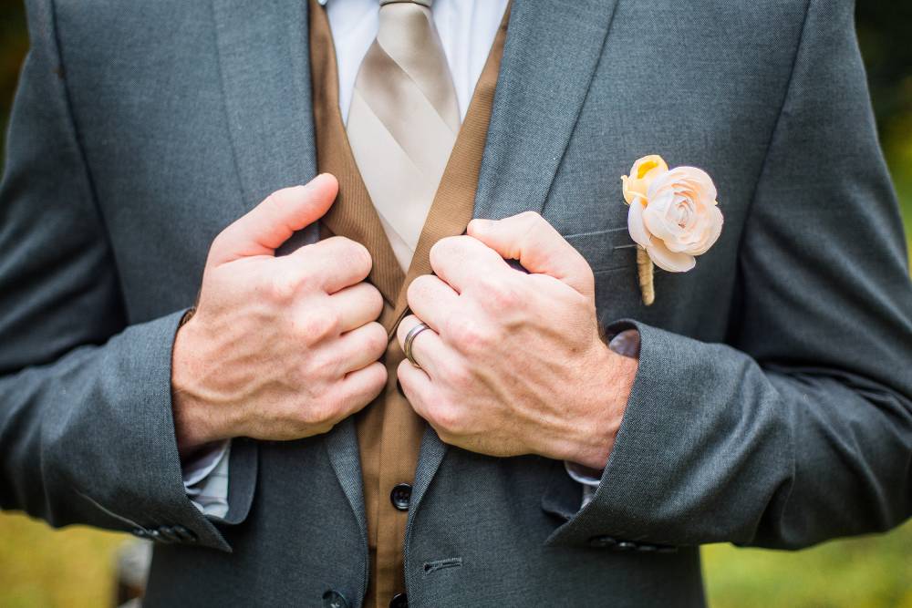 Groom holding jacket with wedding band on hand