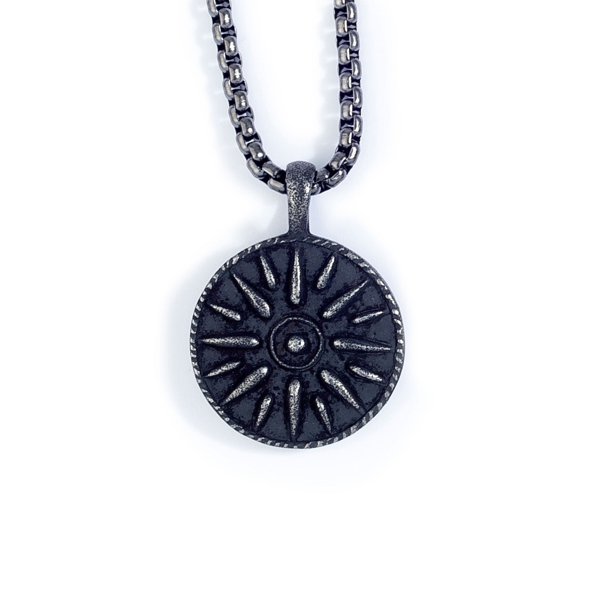 A black stainless steel compass medallion on chain displayed on a neutral white background.
