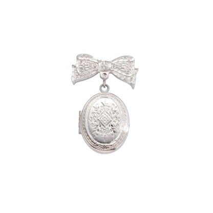 A bow pin and oval locket with bezel inserts displayed on a neutral white background.