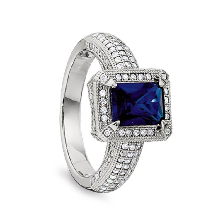 A emerald cut synthetic blue sapphire women's ring with simulated diamonds displayed on a neutral white background.