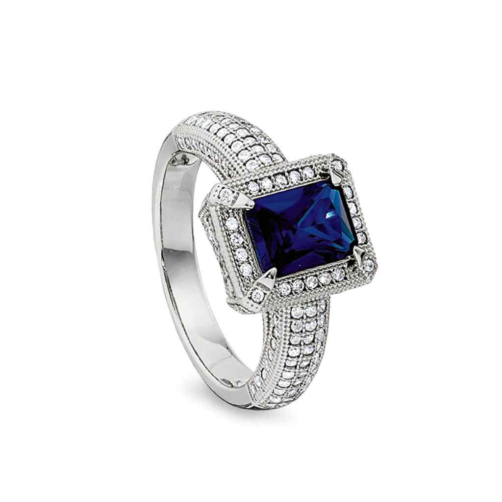 A emerald cut synthetic blue sapphire ring with simulated diamonds displayed on a neutral white background.